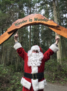 Santa Claus pointing to Wander in Wonder entry arch to Price Sculpture Forest park garden in Coupeville on Whidbey Island