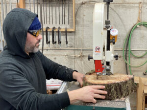 Artist Anthony May using bandsaw to cut log rounds into smaller pieces for Price Sculpture Forest installation