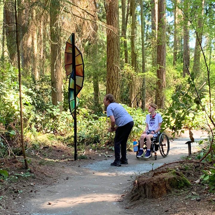 A wheelchair user and companion traveling along a forest trail