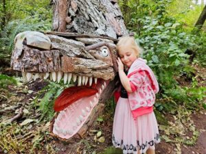 A child exploring a dinosaur sculpture in the forest