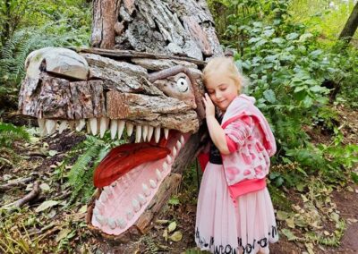 A child exploring a dinosaur sculpture in the forest