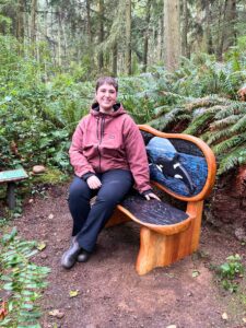 A visitor sitting on a sculptural wooden bench in the forest