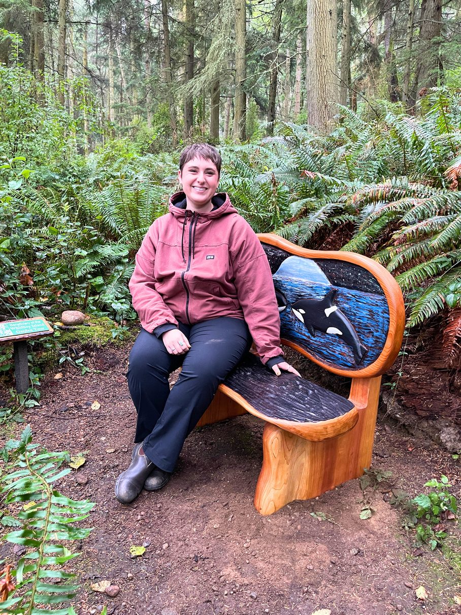 A visitor sitting on a sculptural wooden bench in the forest