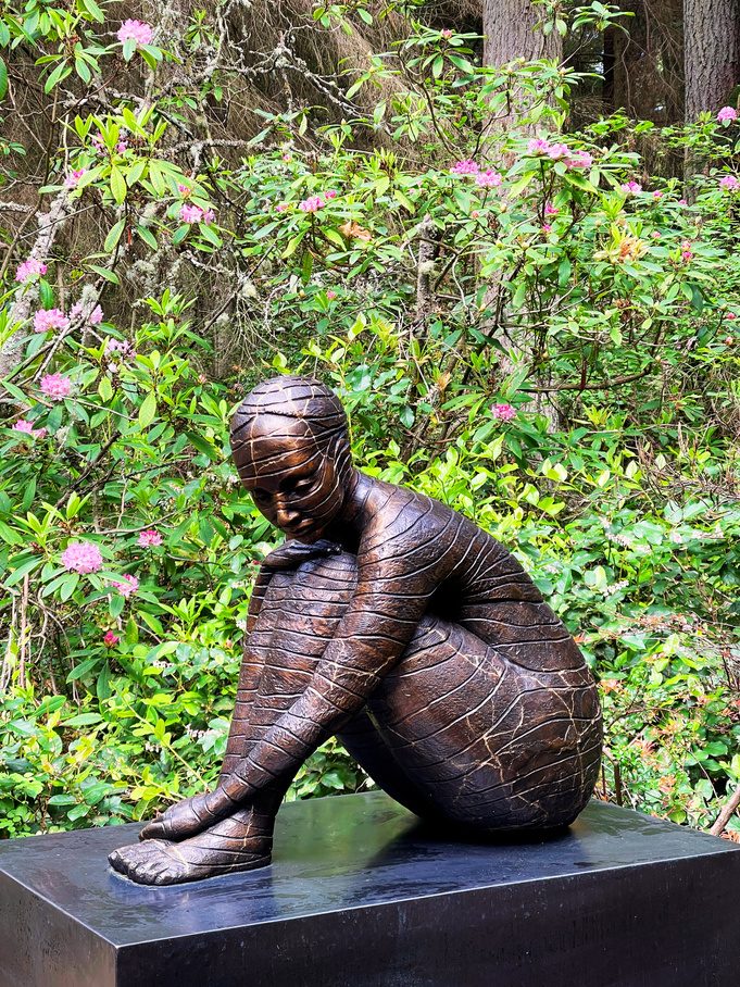 An outdoor figurative sculpture surrounded by forest plants